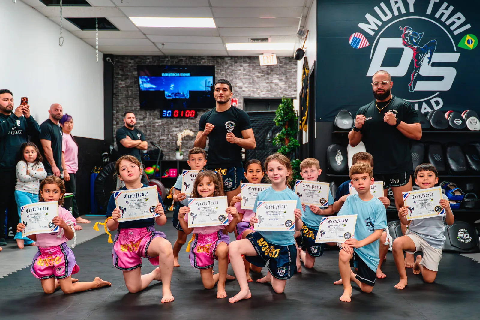 Kids holding their Muay Thai certificates with the coaches